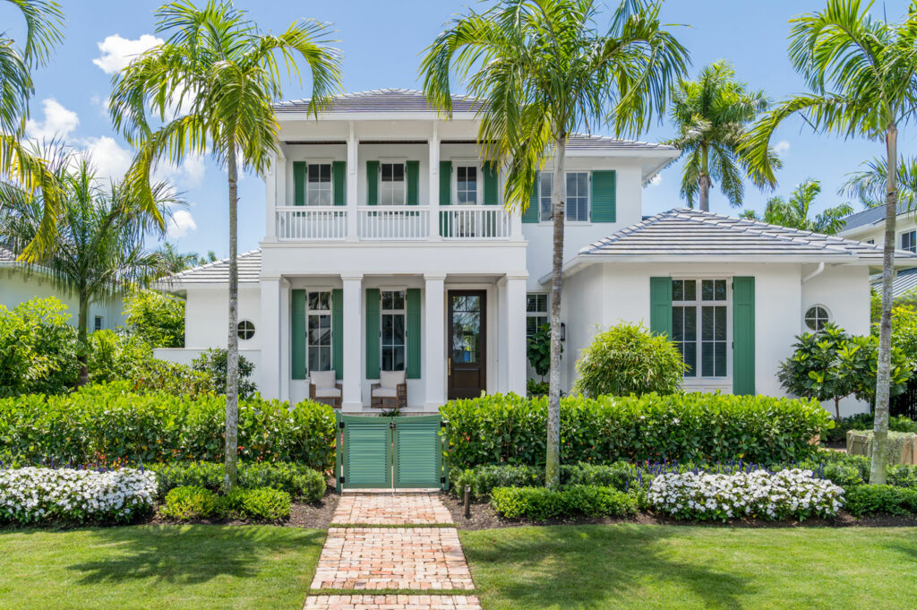 Elegant white two-story house with palm trees and lush greenery.